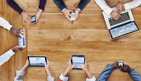 Group of people sitting around a table interacting with their smart devices