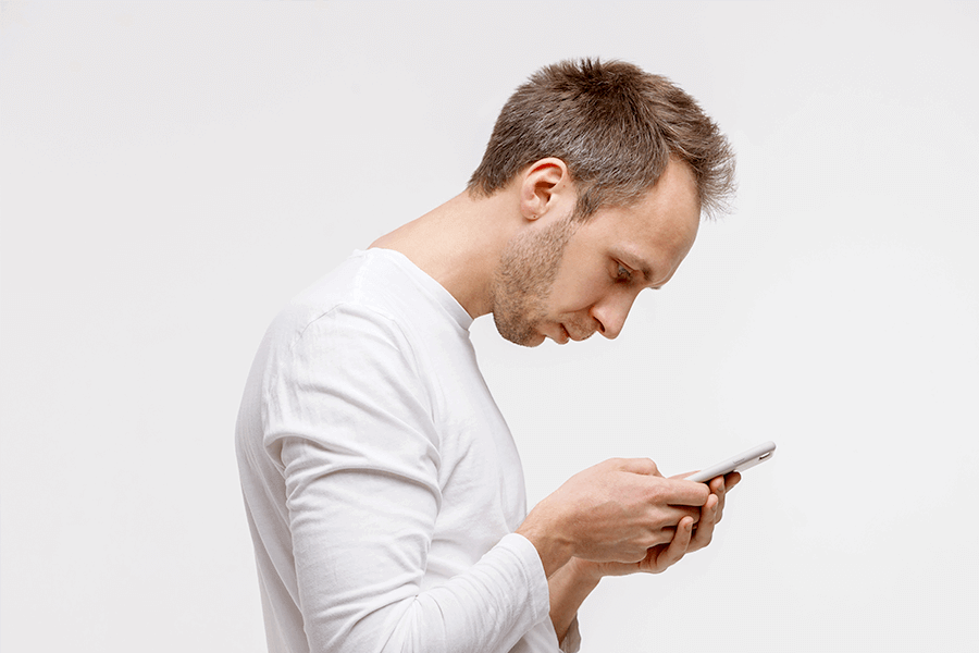 Man hunching over to look at his phone, demonstrating what kyphosis looks like