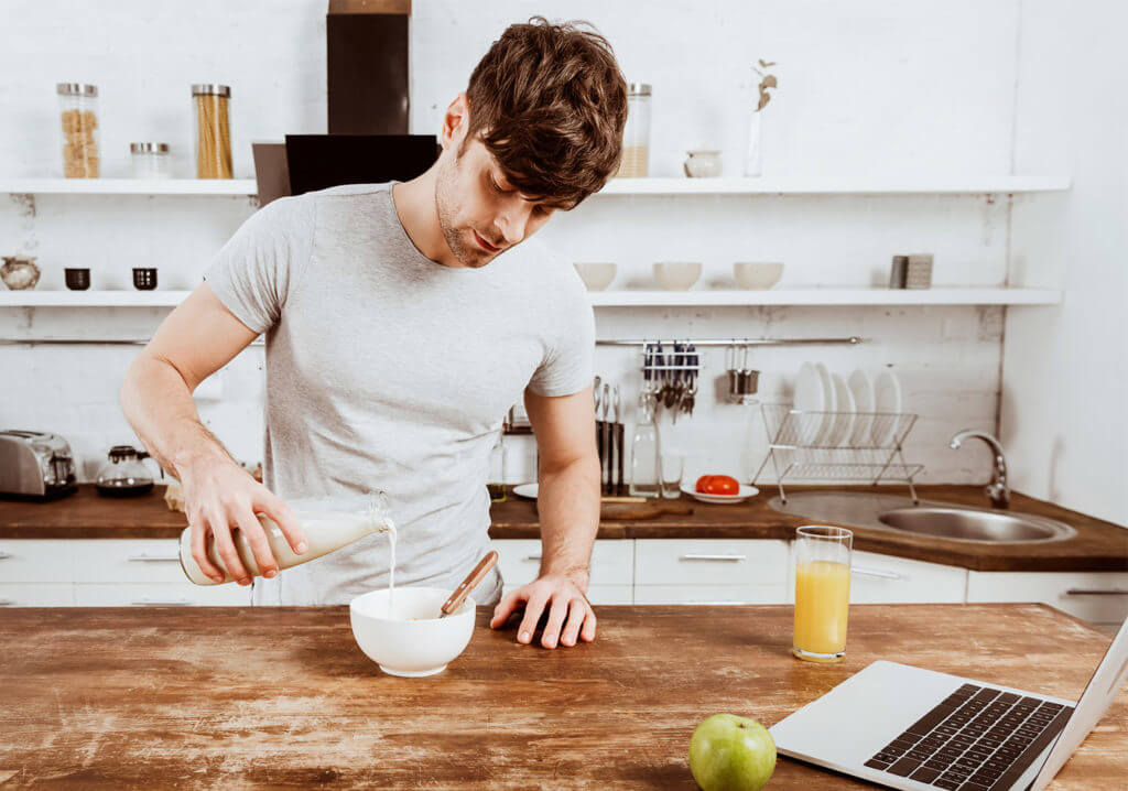 Man hunching over a counter to pour his milk into a bowl