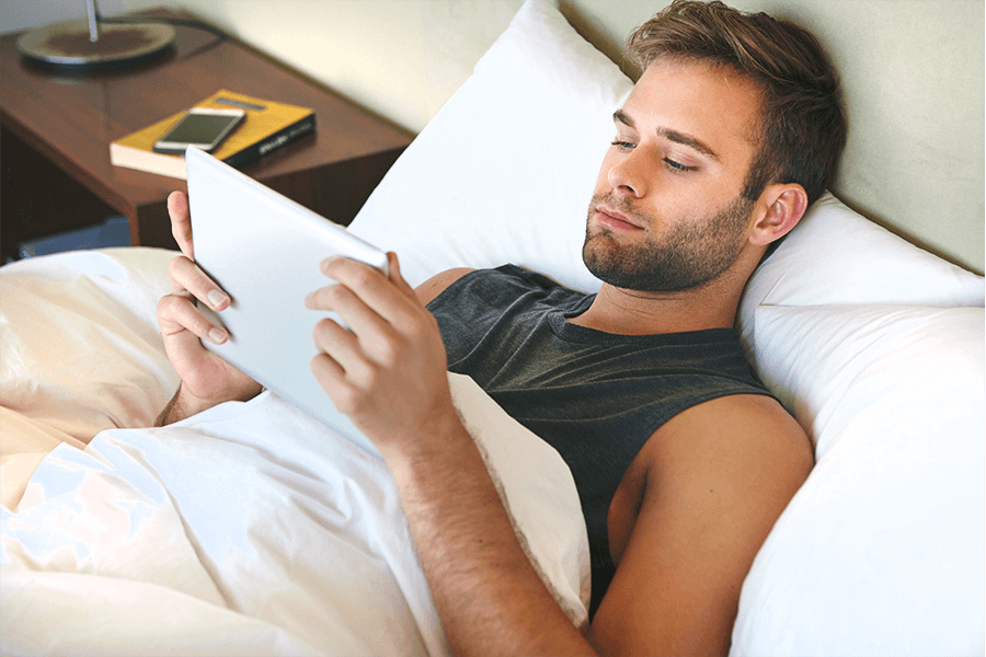 Man laying in his bed looking at a tablet