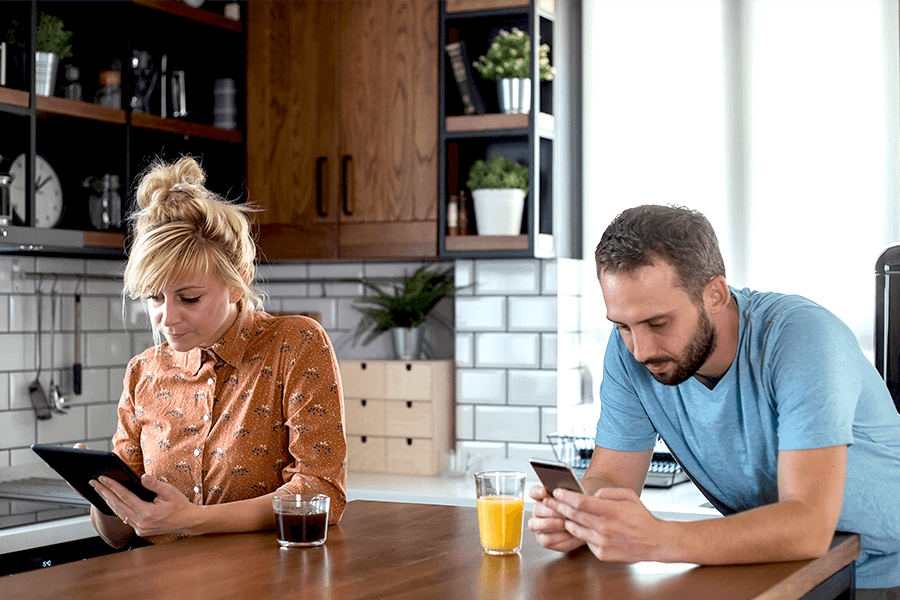 Man and woman in their kitchen looking down at their smartphones