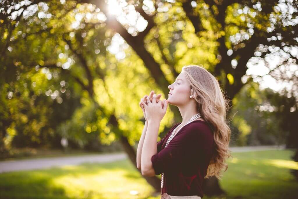 Woman closing her eyes with grasped hands standing outside