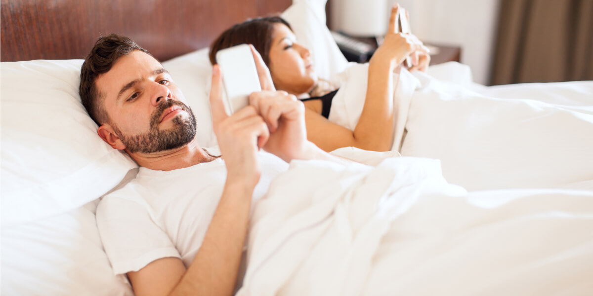 Couple laying in their bed looking at their smartphones