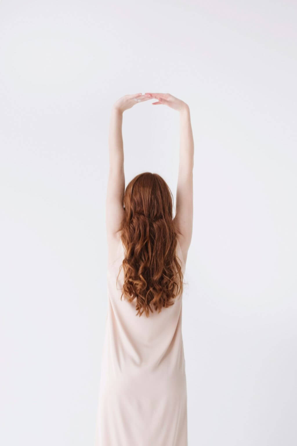 Woman in front of a white wall stretching her arms and back