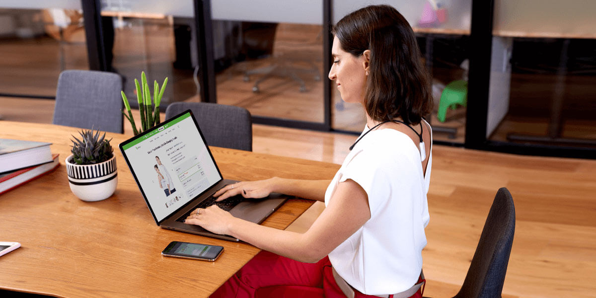 Woman sitting at her desk in an office with her Upright Necklace and device on her back