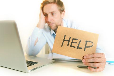 A man looking disappointed at his laptop holding up a help sign
